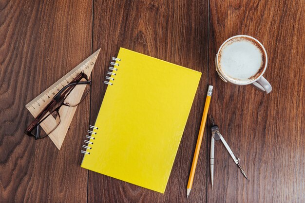 Auf hölzernem Notizbuchbleistift Kaffee und Blumen.