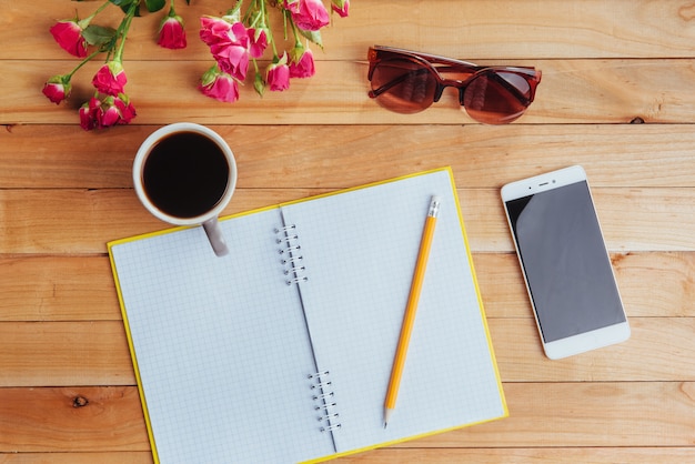 Auf hölzernem Notizbuchbleistift Kaffee und Blumen.