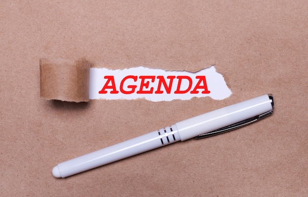 Auf Kraftpapier, ein weißer Stift und ein weißer Papierstreifen mit dem Text AGENDA.