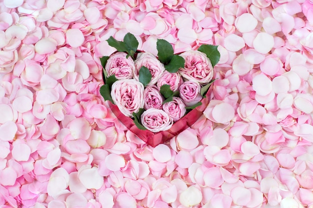 auf rosa Rosenblättern ein Strauß rosa Rosen in einer herzförmigen Geschenkbox