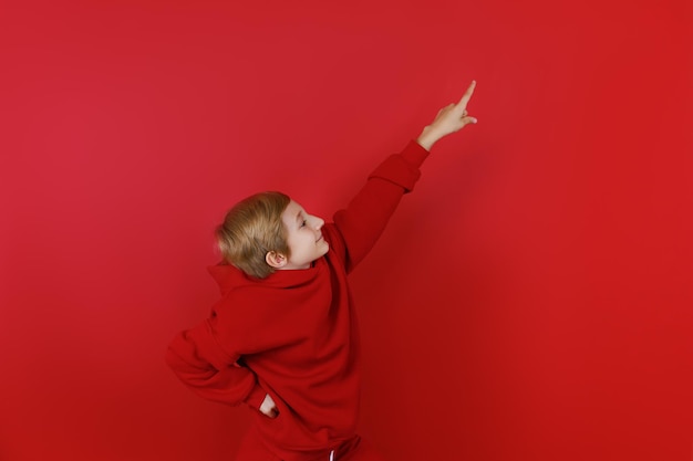 Auf rotem Grund steht ein Junge in einem roten Trainingsanzug und zeigt seine Hand zur Seite