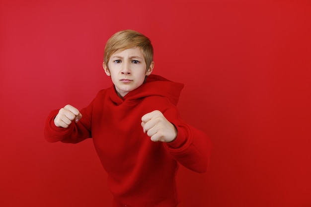 Auf rotem Grund zeigt ein Junge in einem roten Trainingsanzug Drohzeichen
