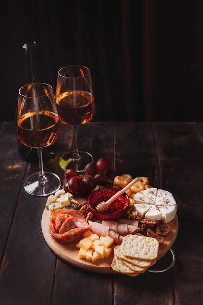 Foto auf rundem brett geschnittene wurst und käse mit fruchtkeksen und soße mit zwei gläsern weißem portwein und einer flasche