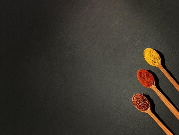 Auf schwarzem Hintergrund drei Holzlöffel mit Gewürzen, Paprika, Chili und Curry-Kurkuma