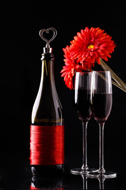 Auf schwarzem Hintergrund Flasche Wein, rote Blume, zwei Weingläser