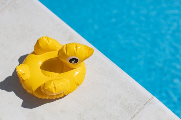 Aufblasbare gelbe Mini-Ente, Cocktail-Ständer nahe Schwimmbad an hellem sonnigem Tag, Kopienraum. Draufsicht.