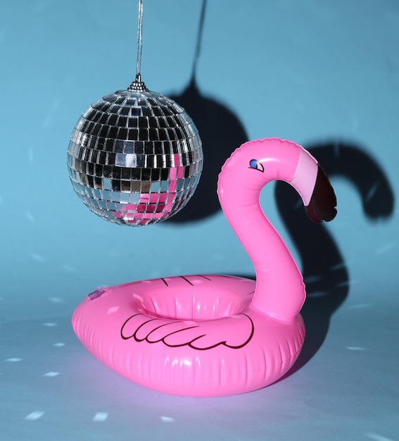 Aufblasbarer Flamingo unter Discokugel auf blauem hellem Hintergrund Minimalistisches Partykonzept