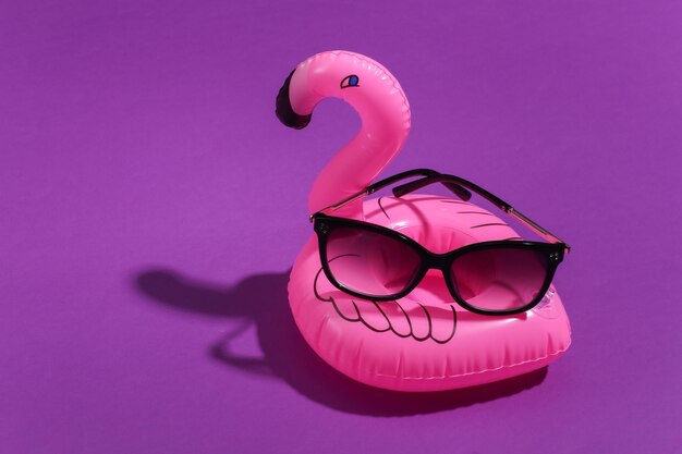 Aufblasbarer rosa Flamingo mit Sonnenbrille auf lila sonnigem Hintergrund. Sommerferienkonzept. Minimalismus