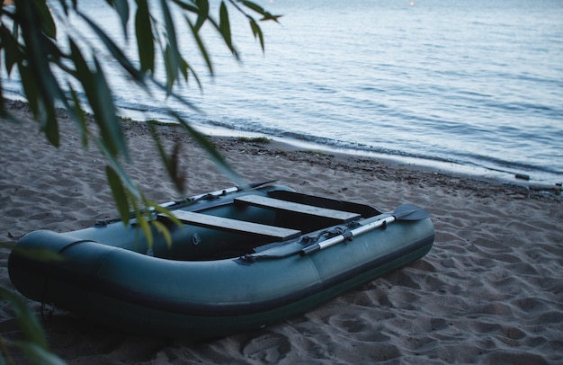 Aufblasbares grünes Boot mit Rudern auf dem Strandsand