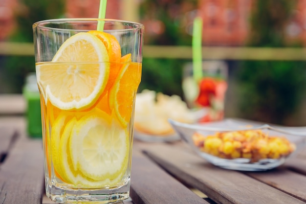 Aufgegossene Fruchtwassercocktails und grüne Gemüsesmoothies über einem Holztisch im Freien. Gesundes Bio-Sommergetränkekonzept.