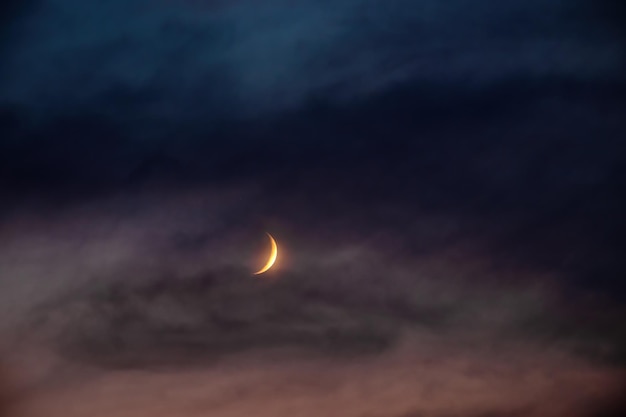 Aufgehender Mond Eine Mondsichel am dunklen bewölkten Nachthimmel