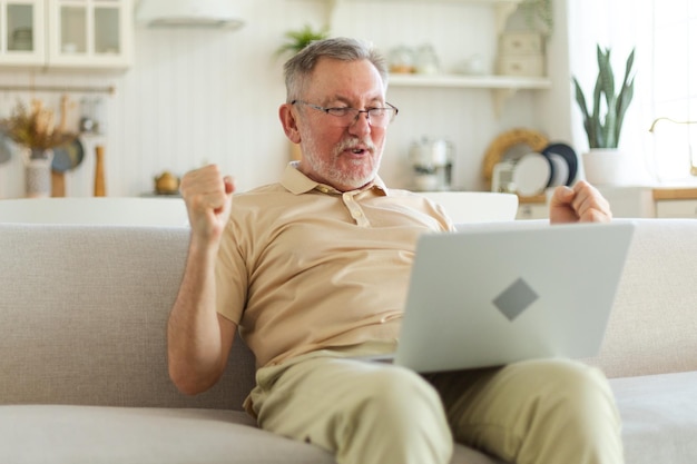 Aufgeregt älterer Mann mittleren Alters, euphorischer Sieger, älterer reifer Großvater, der auf den Laptop blickt und gr. liest