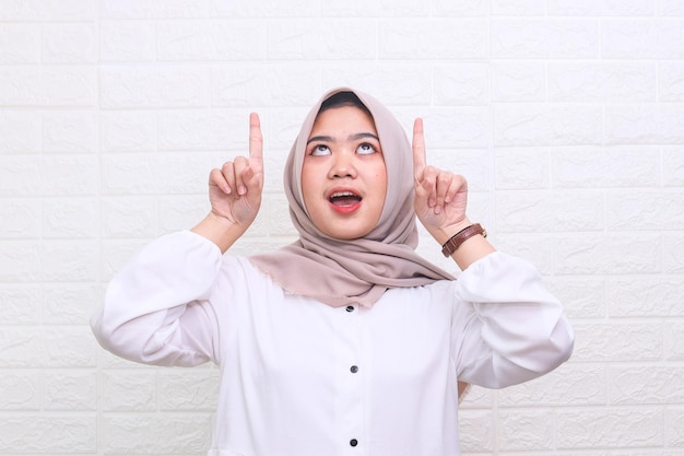 Aufgeregt asiatische muslimische Frau im Hijab, die mit zwei Händen auf den Kopierraum zeigt