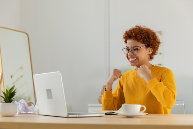 Aufgeregt glückliche afroamerikanische Gewinnerin Studentin schaut auf den Laptop, hat die Prüfung bestanden und tolle Nachrichten gelesen, gute Ergebnisse erzielt und die Online-Ausschreibung gewonnen. Sie ist erstaunt, als sie zu Hause auf den Computer schaut