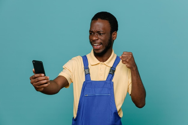 Aufgeregt nehmen Sie ein Selfie junger afroamerikanischer Reinigungsmann in Uniform isoliert auf blauem Hintergrund