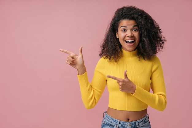 Aufgeregte afroamerikanische Frau, die mit dem Finger auf den Kopienraum zeigt, der auf rosafarbenem Hintergrund isoliert ist