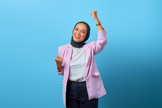 Aufgeregte asiatische Frau, die Erfolg mit Lachenausdruck über blauem Hintergrund feiert