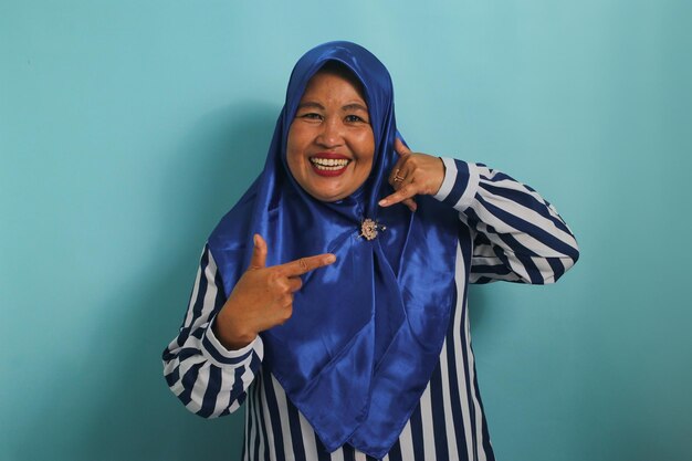 Foto aufgeregte asiatische frau in blauem hijab und gestreiftem hemd macht eine geste, die nach rechts zeigt
