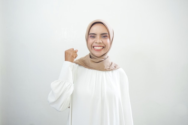 Aufgeregte asiatische muslimische Frau, die den Sieg isoliert über weißem Hintergrund feiert