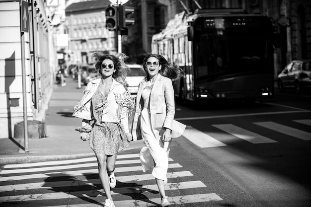 Aufgeregte befreundete Mädchen, die auf dem Zebrastreifen laufen und tolle Zeit zusammen in der Sommerstraßenstadt verbringen.