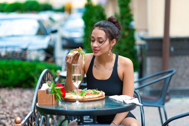 Aufgeregte brünette Frau mit sexy prallen Lippen isst ein Stück Pizza auf der Straße für Text