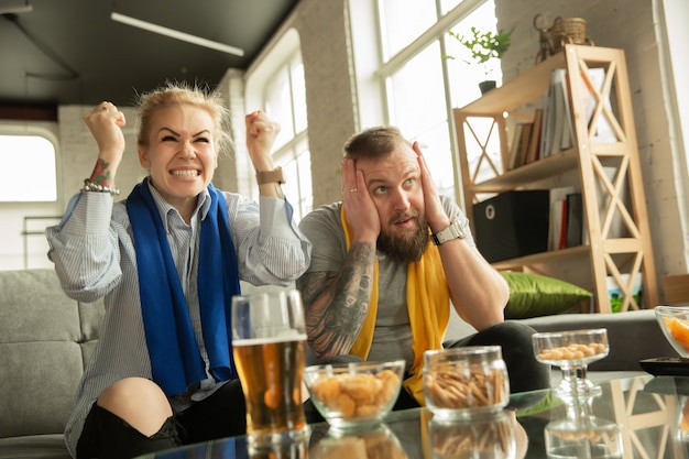 Foto aufgeregte familie, die fußball guckt, sportmatch zu hause. schönes kaukasisches paar, das für nationales basketball-, fußball-, tennis-, fußball-, hockeyteam zujubelt. konzept der emotionen, unterstützung, gefühle.