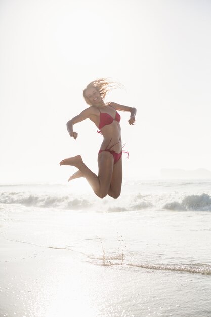 Aufgeregte Frau im Bikini, der auf den Strand springt