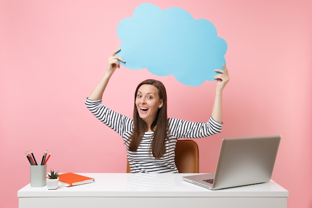 Aufgeregte Frau mit blauem leerem Leerzeichen Sagen Sie Cloud-Sprechblasenarbeit am weißen Schreibtisch mit PC-Laptop