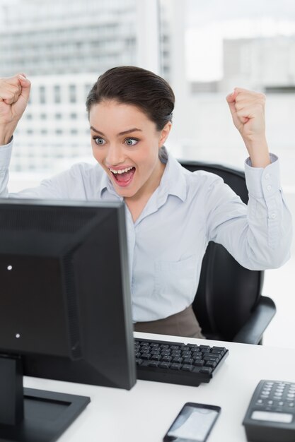 Aufgeregte Geschäftsfrau betrachtet den Bildschirm im Büro