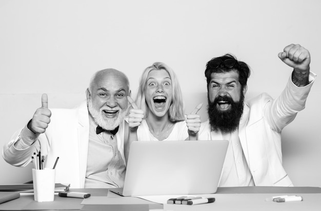 Foto aufgeregte geschäftsleute sitzen am bürotisch mit einer gruppe von kollegen, die an laptops arbeiten