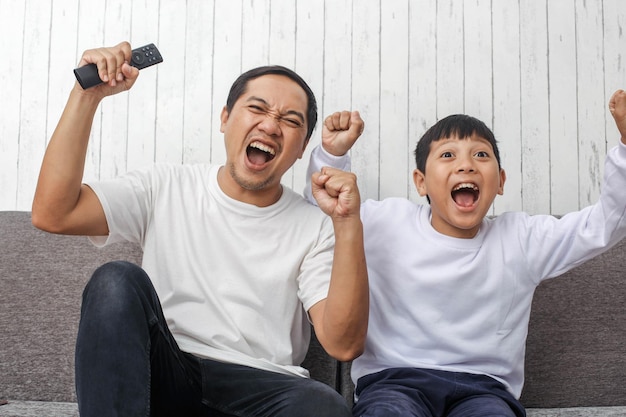 Aufgeregte Gesichtsausdrücke von Vater und Sohn, die zu ihrer Lieblingsfußballmannschaft fernsehen, machen einen