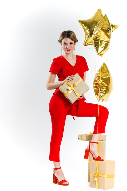 Aufgeregte hübsche blonde Dame im roten Kostüm, die Stapel Geschenkboxen über weißem Studiohintergrund hält. Frauentag, Valentinstag, Geburtstag, Jubiläum feiern. Shopping für Urlaubskonzept