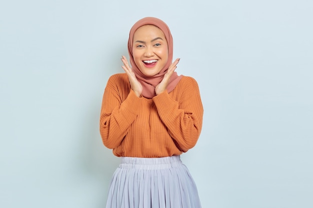 Aufgeregte junge asiatische muslimische Frau im braunen Pullover, die gute Nachrichten isoliert auf weißem Hintergrund erhält Muslimisches Lifestyle-Konzept