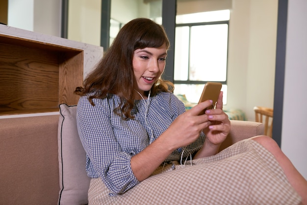 Aufgeregte junge Frau sitzt zu Hause auf dem Sofa und telefoniert mit Freunden von Familienmitgliedern