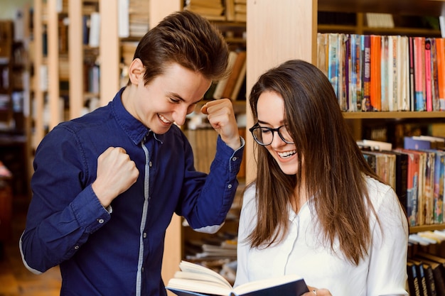 Aufgeregte junge Studenten, die zusammen ein Buch lesen, während sie in der Bibliothek sind