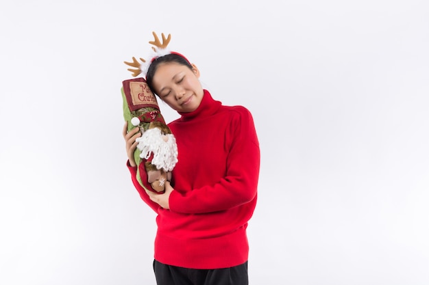 Aufgeregte positive junge Frau im roten Weihnachtsmann-Kostüm mit der Haube, die Präsentkartons hält und den Smartphone lokalisiert verwendet