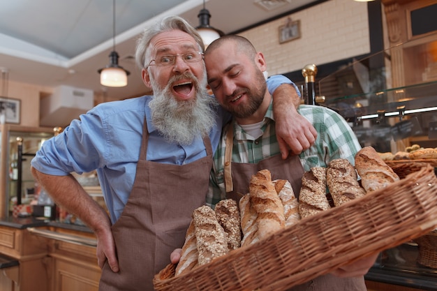 Aufgeregter älterer männlicher Bäcker, der seinen Sohn umarmt, während er zusammen in ihrer Bäckerei arbeitet, die frisches Brot verkauft