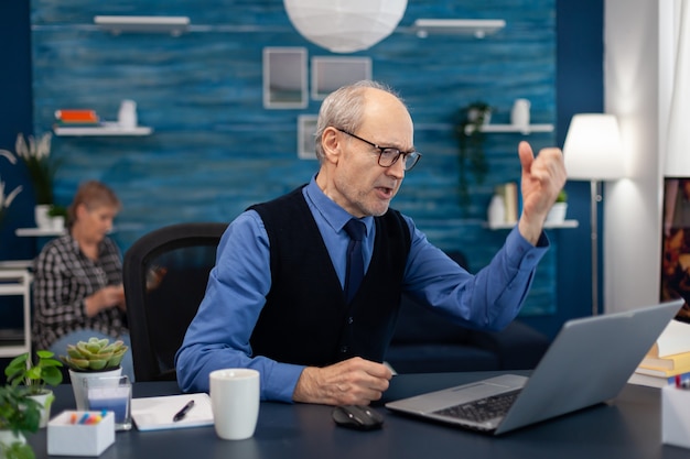 Aufgeregter älterer Mann, der gute Nachrichten feiert, während er vom Homeoffice aus am Laptop arbeitet