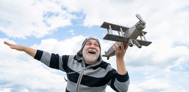 Aufgeregter älterer Mann im Ruhestand reifer Mann im Ruhestand alter Mann auf Himmelshintergrund mit Spielzeugflugzeug