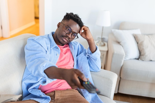 Aufgeregter afroamerikanischer Mann, der den Fernsehcontroller auf die Kamera zeigt, die Kanäle umschaltet, während er fernsieht
