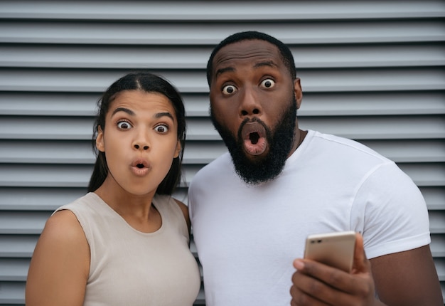 Aufgeregter afroamerikanischer Mann und Frau, die Handy halten, online einkaufen