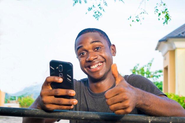 Aufgeregter afroamerikanischer Millennial Junger Mann hält Smartphone in der Hand und fühlt sich euphorisch beim Lesen guter Nachrichten