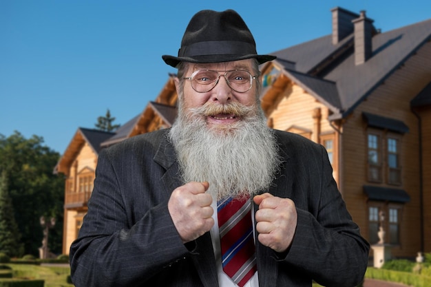 Aufgeregter, fröhlicher alter Mann, der draußen mit geballten Fäusten steht. Schönes Holzhaus im Hintergrund.