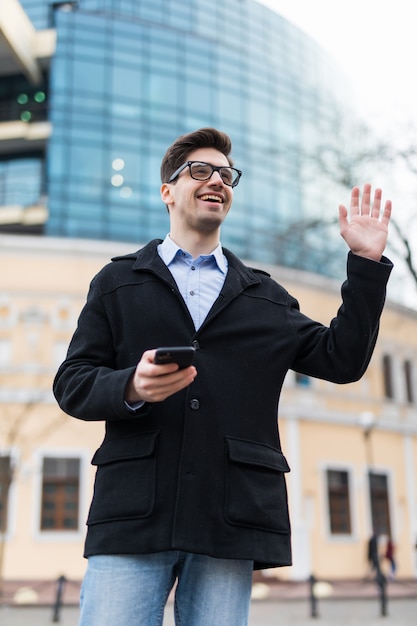 Aufgeregter Geschäftsmann, der seinen Freund mit einer Handbewegung begrüßt und Handy in der Hand hält