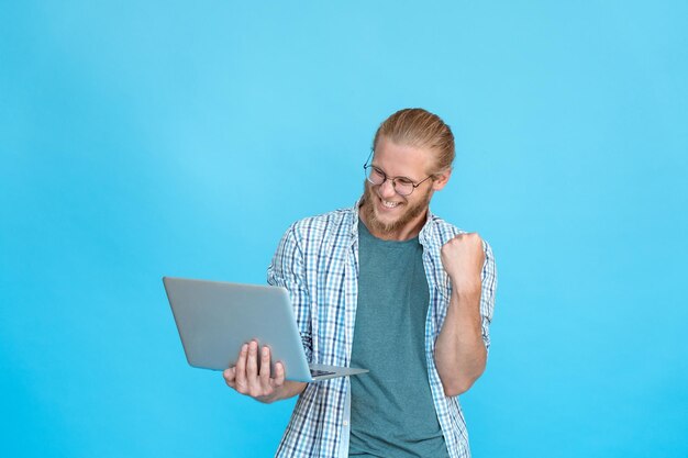 Aufgeregter, glücklicher Geschäftsmann mit Brille hält modernen Laptop in der Hand, ja, Sieger-Sieg-Geste