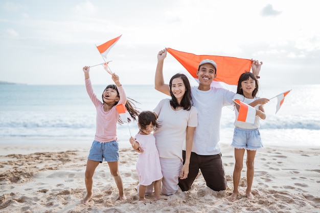 Aufgeregter indonesischer Familienanhänger mit indonesischer Flagge am Strand zusammen