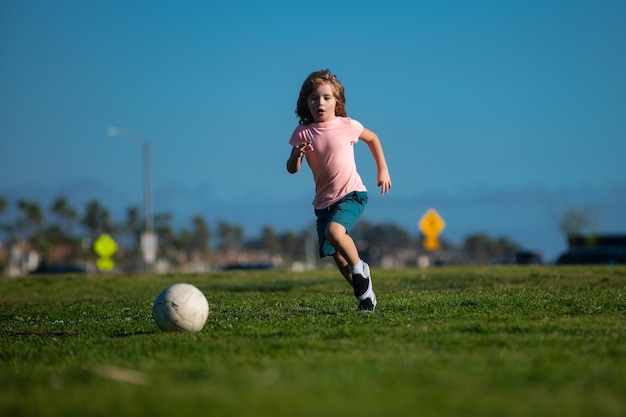 Aufgeregter Junge, der im Freien Ball im Gras tritt Fußballkinder spielen Fußball