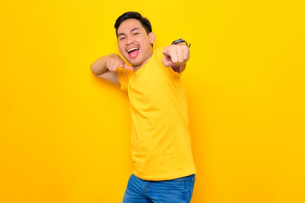 Aufgeregter junger asiatischer Mann in lässigem T-Shirt, der mit beiden Händen auf gelbem Hintergrund isoliert auf die Kamera zeigt Lifestyle-Konzept für Menschen