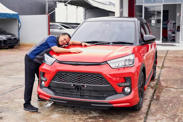 Foto aufgeregter junger, hübscher, asiatischer mann bekommt das neue auto, er umarmt sein auto und ist sehr glücklich.