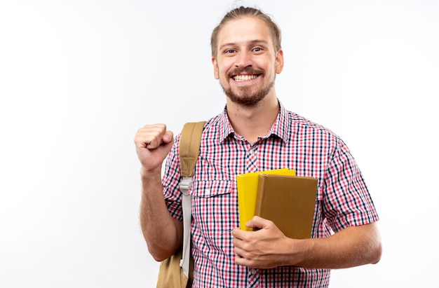 Aufgeregter junger Kerl, der einen Rucksack trägt und Bücher hält, die eine Ja-Geste zeigen, die auf weißer Wand mit Kopienraum isoliert ist?